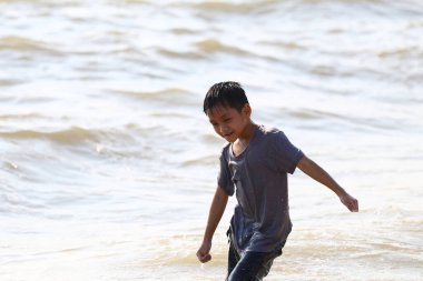 Neşeli bir çocuk sahildeki suya neşeyle su sıçratır, neşeli bir yaz günü eğlence ve keşif sırasında çocukluk mutluluğunun özünü yakalar..