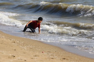 Neşeli genç bir çocuk kumsalda güneşli bir günün tadını çıkarıyor, dalgalarda oynuyor ve etrafı kum ve okyanus esintileriyle çevrili olarak kendini suya daldırıyor..