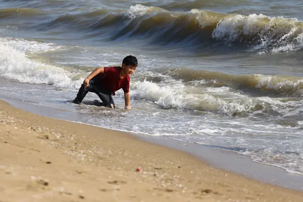 Neşeli genç bir çocuk kumsalda güneşli bir günün tadını çıkarıyor, dalgalarda oynuyor ve etrafı kum ve okyanus esintileriyle çevrili olarak kendini suya daldırıyor..