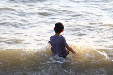 Neşeli bir çocuk, sığ sularda oynamaktan, yazın sıcaklığını ve okyanusun huzurunu hissederken su sıçratmaktan zevk alır..