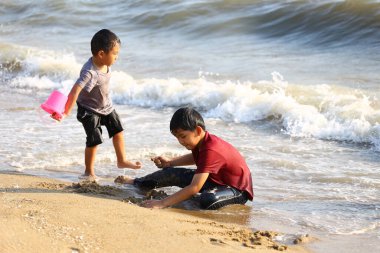 İki çocuk kumsalda eğlenceli ve eğlenceli bir günün tadını çıkarıyorlar. Kumsalda oyun oynuyorlar ve su sıçratıyorlar. Sıcak güneş, okyanusta neşeli anılar yaratırken parlıyor..