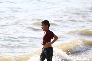 Neşeli bir çocuk sahildeki dalgalarda neşeyle süzülür, çocukluğun saf hazzını ve sahildeki güneşli bir günün enerjisini gösterir..