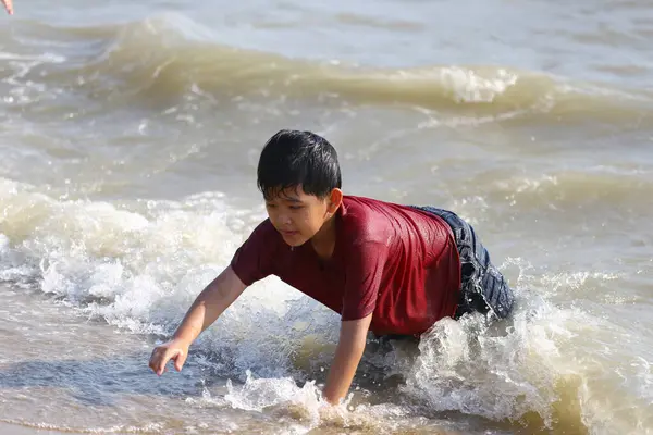 Genç bir çocuk sığ okyanus suyunda neşeyle sürünüyor, su sıçratıyor ve sahilde oynuyor. Parlak güneş sonsuz yaz eğlencesi için neşeli bir atmosfer yaratır..