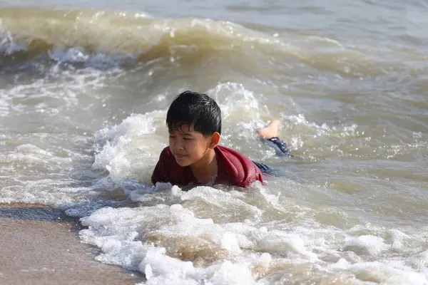 Genç bir çocuk kumsalda narin okyanus dalgalarında neşeyle oynar, çocukluk mutluluğunun ve güneşli bir günde doğanın güzelliğini yakalar..