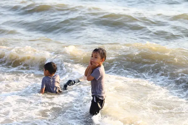 İki genç çocuk, hafif dalgalar ve güneş ışığıyla çevrili sığ okyanus sularında neşeyle oynuyorlar. Çocukluk mutluluğu ve maceranın özünü yakalıyorlar..