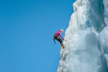 Donmuş bir şelalede buz tırmanışı ekipmanıyla dağcı kadın.