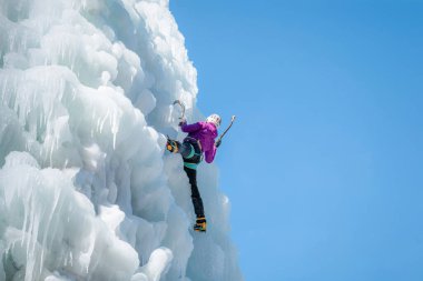 Donmuş bir şelalede buz tırmanışı ekipmanıyla dağcı kadın.