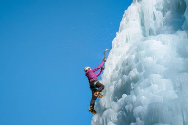 Donmuş bir şelalede buz tırmanışı ekipmanıyla dağcı kadın.
