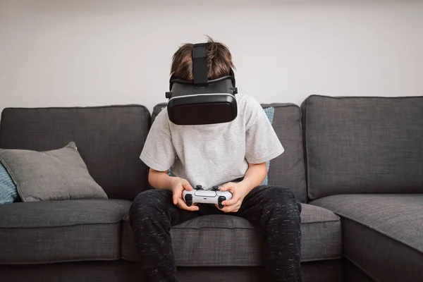 Caucasian boy enjoying at home, gaming using VR box, virtual reality goggles, and simulator, moving and physically interacting with a virtual world
