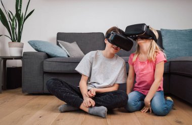 Hayret verici çocuklar evde oturma odasında oyun oynarken sanal gerçeklik gözlüğü kullanıyorlar. Erkek ve kız kardeş