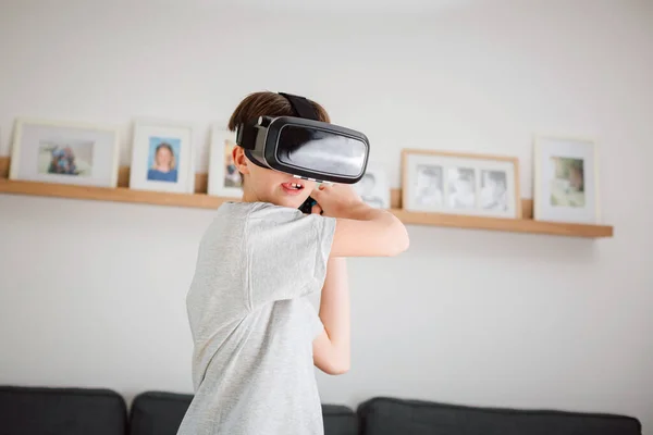 Boy child playing swordplay video games at home, wearing virtual reality vr headset and holding remote controller