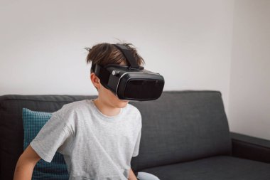 Kafkasyalı erkek çocuk sanal gerçeklik kulaklığı takıyor, sanal dünyaya şaşırmış ve şaşırmış görünüyor.