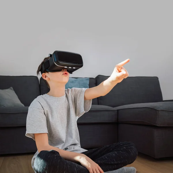 Caucasian school aged boy enjoying new technology at home, using VR goggles, and interacting with objects in a virtual world