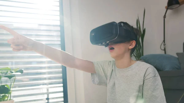Thrilled boy experiencing the virtual world by using a virtual reality headset looking around and pointing finger