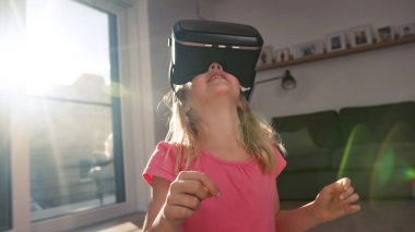 Evde sanal gerçeklik deneyimi sırasında VR kulaklıklı genç bir kız havaya dokunuyor. Artırılmış gerçekliği keşfeden duygusal çocuk.