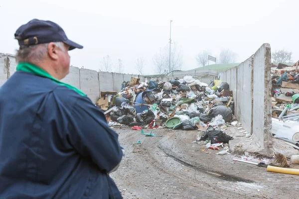 Recycling center worker, in dark blue work clothes, looking at an unsorted garbage heap just arrived in the materials recovery facility, rear view.
