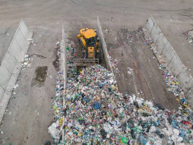 Wheel loader doing a job at waste management plant, using scrap grapple bucket to organize heap of solid garbage, aerial shot.