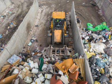 Front loader with scrap handling grapple bucket moving forward and backward to push, scoop and dump material at recycling and waste center