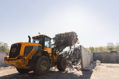 Heavy construction machine, front end loader moving along recycling center area, close up view. Waste management industry concept.