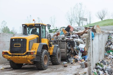Front loader with scrap handling grapple bucket moving forward and backward to push, scoop and dump material at recycling and waste center
