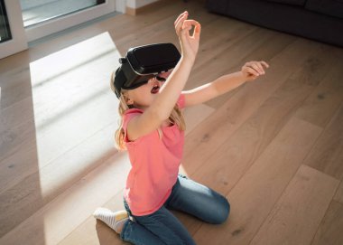 Cheerful blonde female child smiling and enjoying in virtual reality world using VR glasses. Children, technology and development concept.