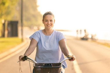 Happy smiling woman riding bicycle along the coast at summer