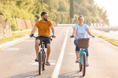 Caucasian couple taking pleasure in the ride on beach cruiser bikes, pedaling on a wonderful route near the sea