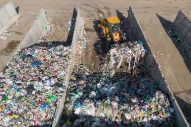 Skid steer loader moving plastic garbage with scrap grapple on the landfill site, drone shot. Waste disposal concept.