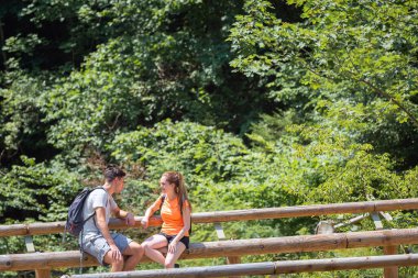 Young couple sitting and relaxing on the mountain river shore, enjoying nature and a sunny summer day. Concept of the romantic weekend and active pastime.