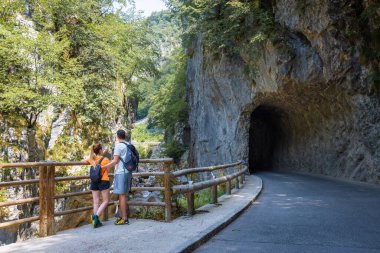 Two young hikers with backpacks, a couple in love standing on the bridge and looking at the steep rocky stream bed