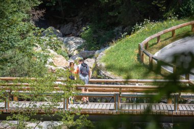 Two young hikers with backpacks, a couple in love standing on the bridge and looking at the steep rocky stream bed