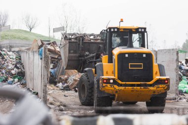 Heavy construction machine, front end loader moving along recycling center area, close up view. Waste management industry concept.