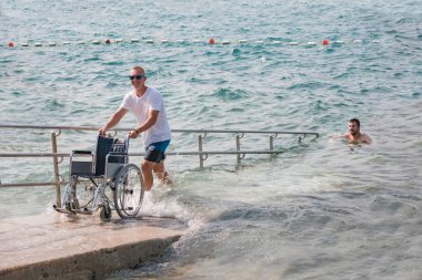 Tekerlekli sandalyedeki engelli adam kumsalda yüzmeye gider..
