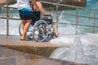 Tekerlekli sandalyedeki engelli adam kumsalda yüzmeye gider..