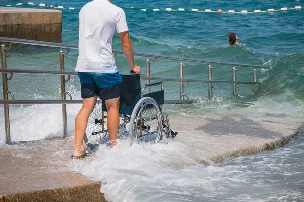 stock image Lifeguard pushing wheelchair at sea on accessible beach with ramp for persons with disability