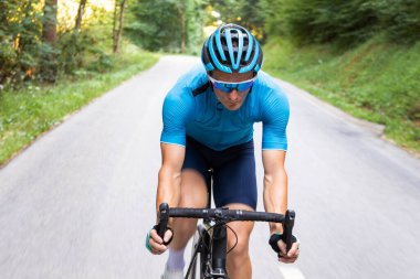 Yarış bisikletinde pedal çeviren bir adam vücut pozisyonunda, kolları ve elleri damlalarda gidonun üzerinde duruyor.