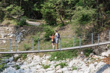 Aktif genç yürüyüşçüler, kadın ve erkek büyük kayaların arasında akan bir dağ deresinin üzerinde yürüyorlar. Doğa keşfi kavramı.