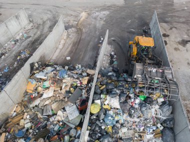 Wheeled loader operating on landfill site, carrying and dumping waste materials using a bucket, aerial high angle shot.