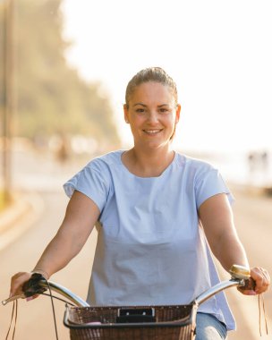 Happy smiling woman riding bicycle along the coast at summer