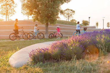 Young family with two children cycling at the city park in summer sunset
