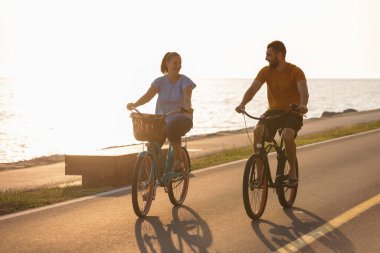 Sahil bisikletleriyle gezmekten zevk alan çift deniz kenarında harika bir yolda pedal çeviriyor.