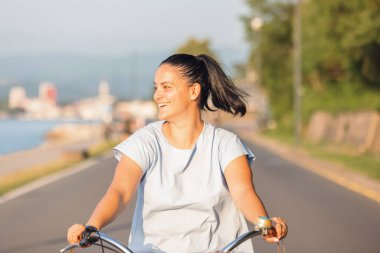 Günbatımında bisiklet süren kaygısız bir kadın eğleniyor ve gülümsüyor.