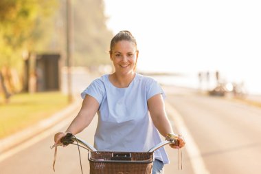 Günbatımında bisiklet süren kaygısız bir kadın eğleniyor ve gülümsüyor.