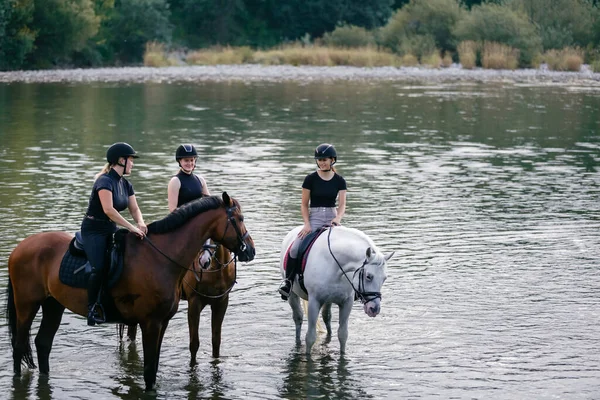 stock image Three young women enjoying equestrian leisure, nature, and river, smiling while sitting on horses