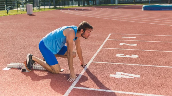 Sideways view male professional athlete preparing beyond start line in a starting block and running