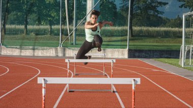 Genç şişman kadın güneşli bir yaz gününde atletizm pistinde koşuyor ve engellerin üzerinden atlıyor.