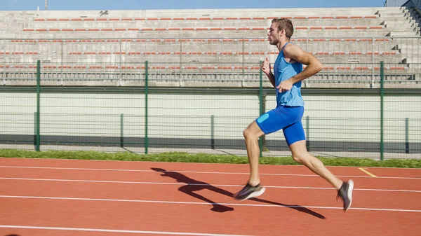 Stadyumdaki atletizm pistinde koşan beyaz tenli profesyonel bir yarışçı..