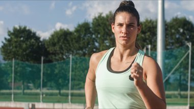 Bir atletizm pistinde orta atletizm eğitiminde odaklanmış güçlü bir beyaz kadın koşucu..