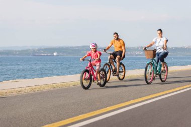 Mother, father and girl child having fun on vacation cycling near the sea. Family coastal bike ride.