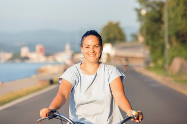 Happy smiling woman riding bicycle along the coast at summer